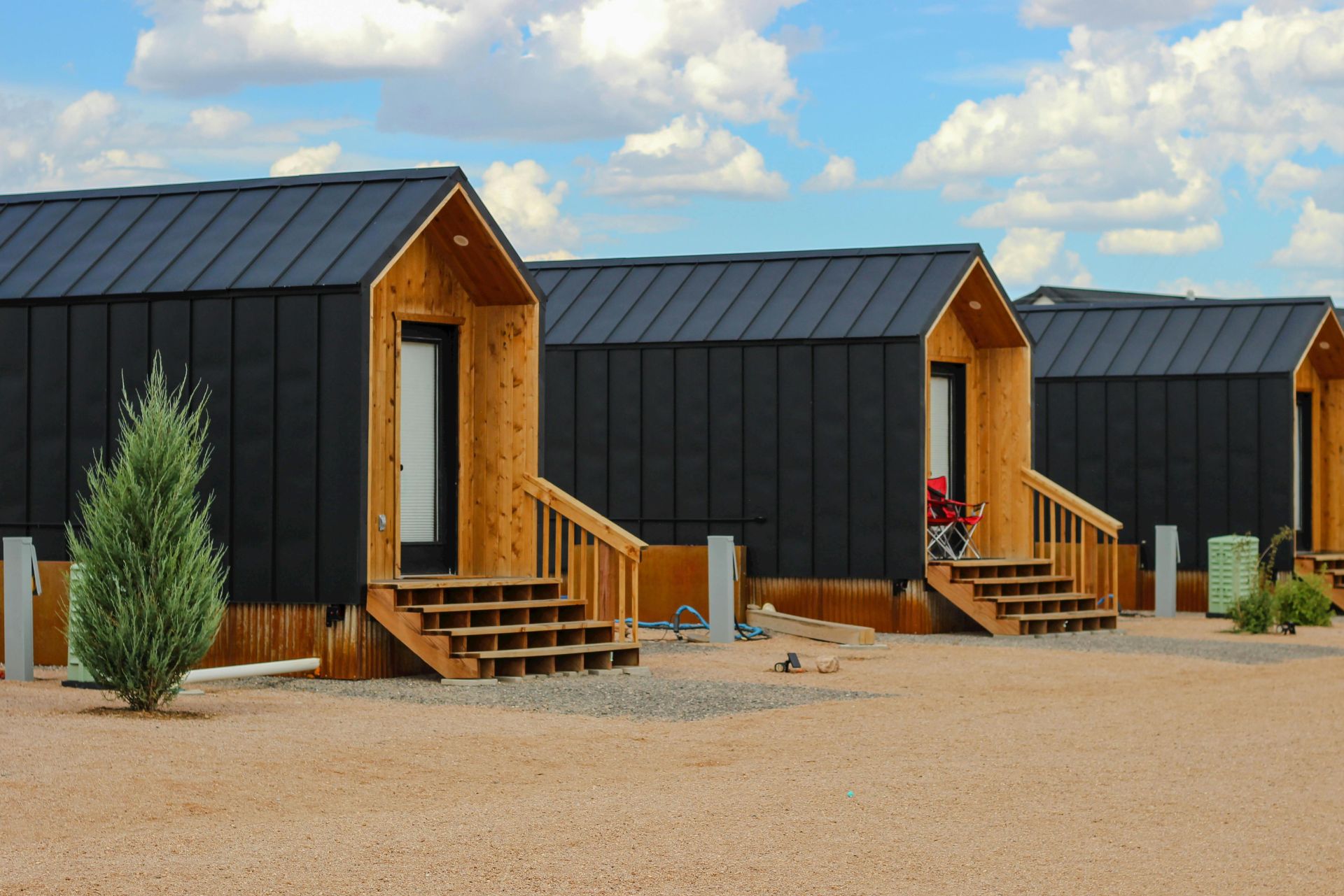 Row of modern black tiny houses in a desert setting under a cloudy sky.