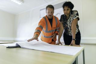 Two engineers reviewing blueprints in an office, discussing project details.