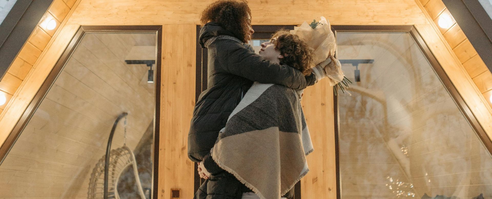 Loving couple embracing in front of a cozy A-frame cabin during winter.